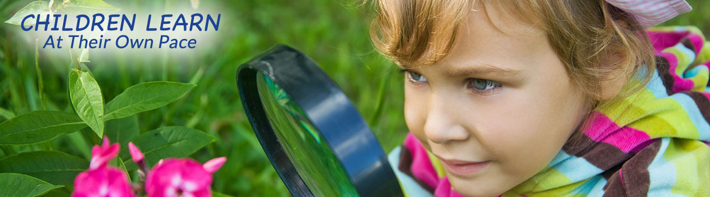 Child looking at a flower through a magnifying glass with words - Children learn at their own pace